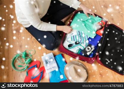 winter holidays, vacation, tourism and objects concept - close up of woman packing travel bag with summer clothes, camera and city guide over snow