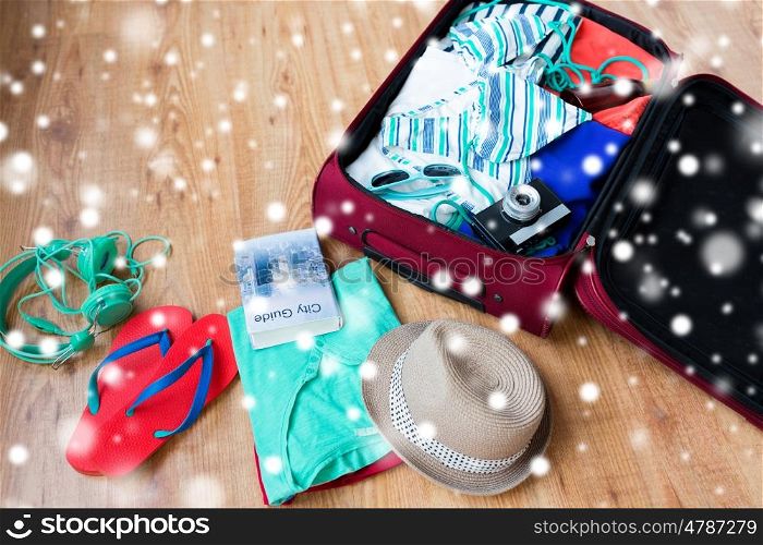 winter holidays, vacation, tourism and objects concept - travel bag with summer clothes, camera and city guide