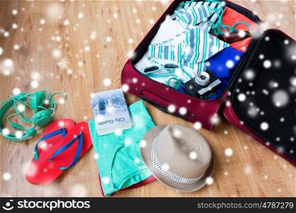 winter holidays, vacation, tourism and objects concept - travel bag with summer clothes, camera and city guide