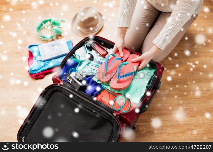 winter holidays, vacation, tourism and people concept - close up of woman packing bag with summer clothes and travel stuff over snow