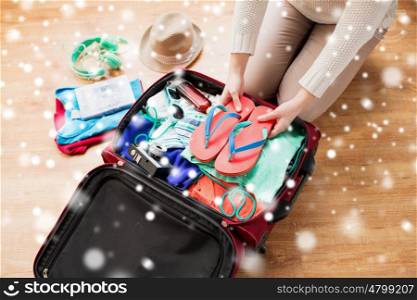winter holidays, vacation, tourism and people concept - close up of woman packing bag with summer clothes and travel stuff over snow
