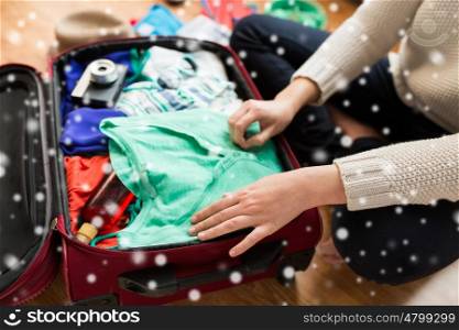 winter holidays, vacation, travel, tourism and objects concept - close up of woman packing bag with summer clothes over snow