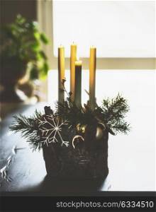 Winter home decoration and festive atmosphere with burning candles, fir branches and snowflakes on table in living room at window. Decorated Fourth Advent wreath