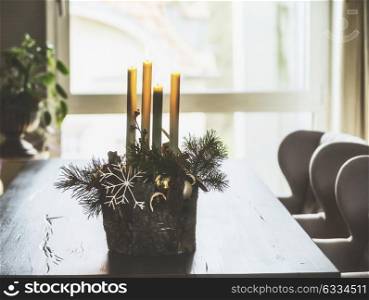 Winter home decoration and festive holiday atmosphere with burning candles, fir branches and snowflakes on table in living room at window. Decorated Advent wreath