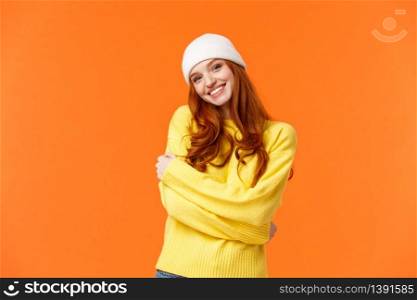 Winter is her favorite season. Tender silly and lovely redhead girl embrace herself and tilt head, smiling cute, wearing beanie and soft warm sweater just for cold weather, orange background.. Winter is her favorite season. Tender silly and lovely redhead girl embrace herself and tilt head, smiling cute, wearing beanie and soft warm sweater just for cold weather, orange background