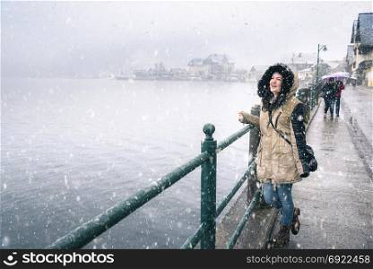 Winter joy theme image with a young woman laughing and enjoying the snowfall, on the Hallstatter See shore, in the famous Hallstatt town, in Austria.