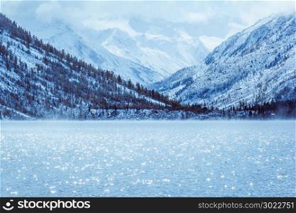 Winter lake with snow-covered pines on the Bank of the rocky mountains. The Altai mountains, fog over the winter lake.
