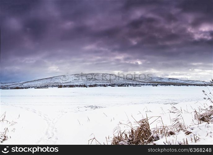 Winter landscape, frozen lake in snow and ice. Snow covered fields on the hills