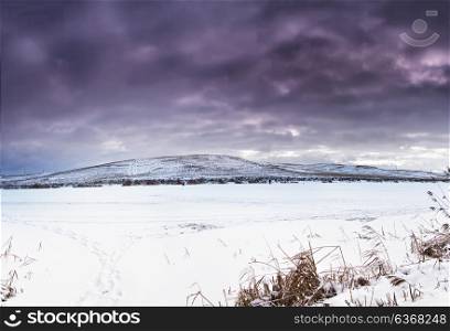 Winter landscape, frozen lake in snow and ice. Snow covered fields on the hills