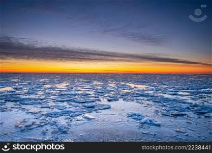 Winter landscape in beach, coastline with cracked ice, snow and opened sea water on sunset.
