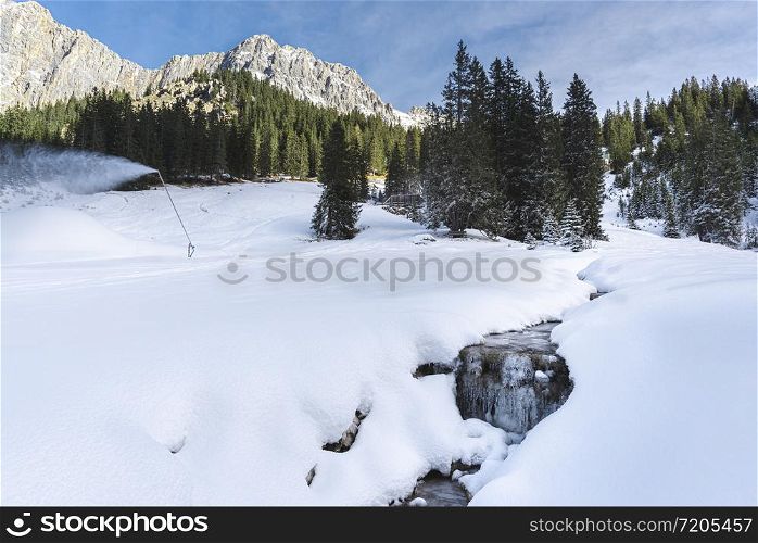 Winter landscape in the Austrian Alps. Frozen creek surrounded by snowdrifts and snowy pine trees.