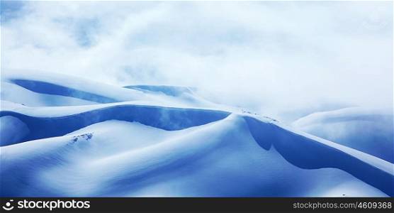 Winter landscape of high mountains with snow blizzard and fresh blue sky, beautiful nature panoramic image
