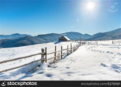 Winter landscape with a old rural house on white snow with blue sky and shining sun