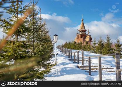 Winter landscape with a wooden orthodox church on the hill and wooden stairs under snow leading up to it. Waterfall Gremiachy near Sergiev Posad, Russia