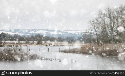 Winter landscape with snow falling and covering ground and foliage in English countryside