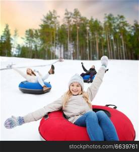 winter, leisure and entertainment concept - group of happy friends sliding down hill on snow tubes over natural background. happy friends sliding down hill on snow tubes