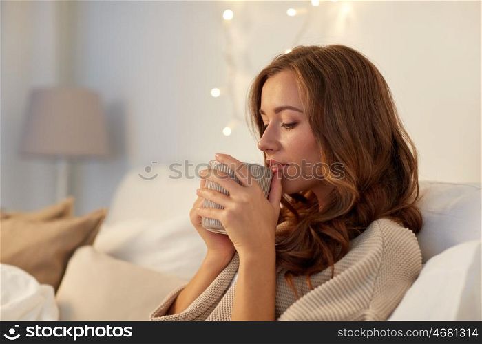 winter, leisure and people concept - happy young woman with cup of coffee or tea in bed at home bedroom