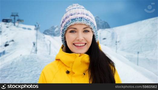 winter, leisure, clothing and people concept - happy young woman in winter clothes over downhill skiing and mountains background