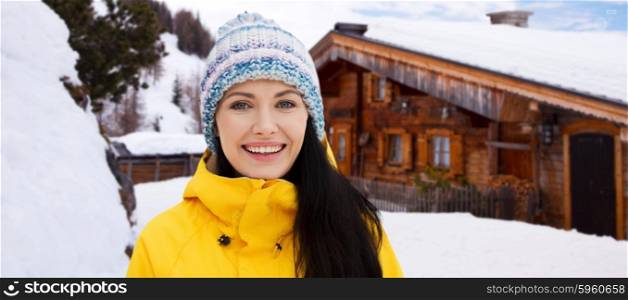 winter, leisure, clothing and people concept - happy young woman in winter clothes outdoors over wooden country house background and snow