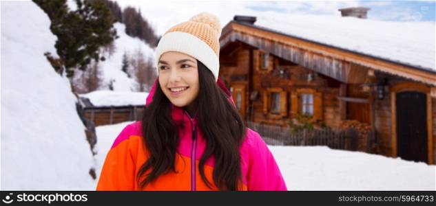winter, leisure, clothing and people concept - happy young woman or teenage girl in winter clothes outdoors over wooden country house background and snow