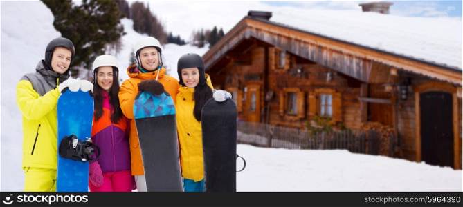 winter, leisure, extreme sport, friendship and people concept - happy friends in helmets with snowboards outdoors over wooden country house background and snow