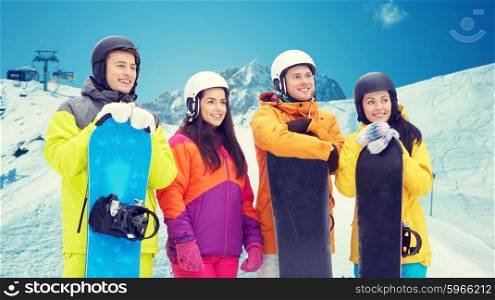 winter, leisure, extreme sport, friendship and people concept - happy friends in helmets with snowboards over snow and mountain background