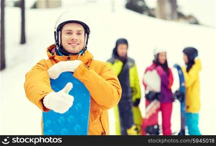winter, leisure, extreme sport, friendship and people concept - happy young man in helmet with snowboard and group of friends showing thumbs up