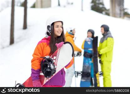winter, leisure, extreme sport, friendship and people concept - happy young woman in helmet with snowboard and group of friends