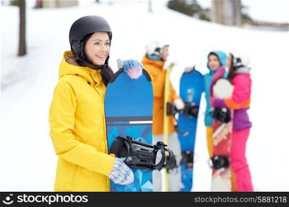 winter, leisure, extreme sport, friendship and people concept - happy young woman in helmet with snowboard and group of friends