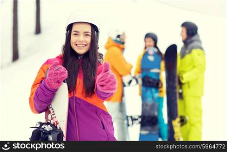 winter, leisure, extreme sport, friendship and people concept - happy young woman in helmet with snowboard and group of friends showing thumbs up