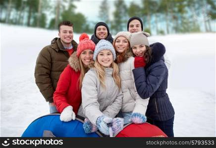 winter, leisure, friendship, technology and people concept - group of smiling young men and women with snow tubes taking picture with smartphone selfie stick outdoors
