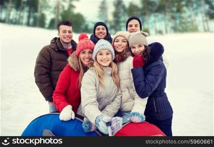 winter, leisure, friendship, technology and people concept - group of smiling young men and women with snow tubes taking picture with smartphone selfie stick outdoors