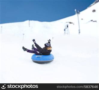 winter, leisure, sport, and people concept - happy teenage boy or young man sliding down on snow tube over mountain background