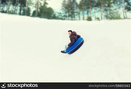 winter, leisure, sport, and people concept - happy teenage boy or young man sliding down on snow tube