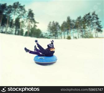 winter, leisure, sport, and people concept - happy teenage boy or young man sliding down on snow tube