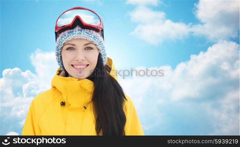 winter, leisure, sport and people concept - happy young woman in ski goggles over blue sky and clouds background