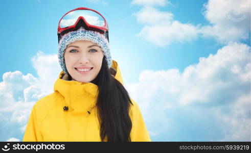 winter, leisure, sport and people concept - happy young woman in ski goggles over blue sky and clouds background