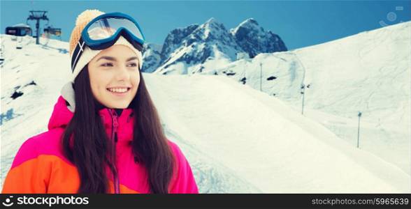 winter, leisure, sport and people concept - happy young woman in ski goggles over snow and mountain background
