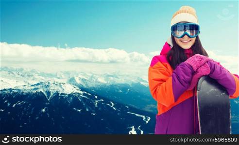 winter, leisure, sport and people concept - happy young woman in ski goggles with snowboard over snowy mountain background