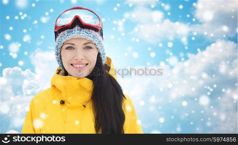 winter, leisure, sport and people concept - happy young woman in ski goggles over blue sky and clouds background