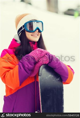 winter, leisure, sport and people concept - happy young woman in ski goggles with snowboard outdoors
