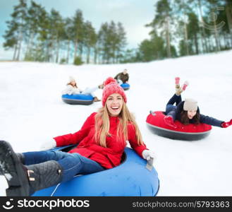 winter, leisure, sport, friendship and people concept - group of happy friends sliding down on snow tubes