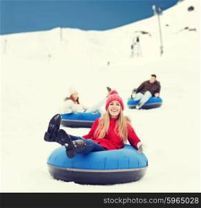 winter, leisure, sport, friendship and people concept - group of happy friends sliding down on snow tubes over mountain background