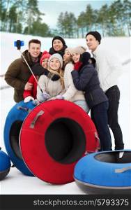 winter, leisure, sport, friendship and people concept - group of smiling friends with snow tubes taking picture by smartphone selfie stick outdoors