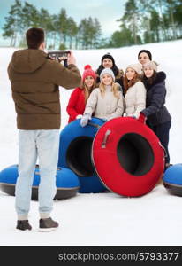 winter, leisure, sport, friendship and people concept - group of smiling friends with snow tubes taking picture by tablet pc computer outdoors