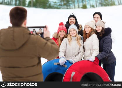 winter, leisure, sport, friendship and people concept - group of smiling friends with snow tubes taking picture by tablet pc computer outdoors