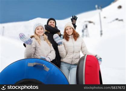 winter, leisure, sport, friendship and people concept - group of smiling friends with snow tubes waving hands over mountain background