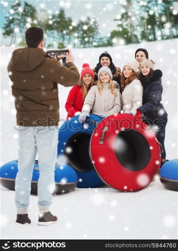 winter, leisure, sport, friendship and people concept - group of smiling friends with snow tubes taking picture by tablet pc computer outdoors