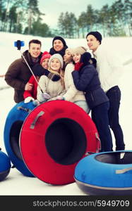 winter, leisure, sport, friendship and people concept - group of smiling friends with snow tubes taking picture by smartphone selfie stick outdoors