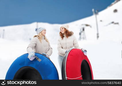 winter, leisure, sport, friendship and people concept - happy girl friends with snow tubes outdoors over mountain background